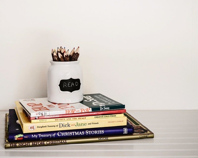 Pot of colouring pencils on top of a pile of books.