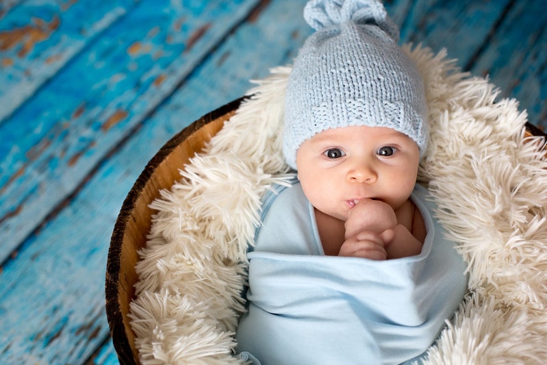 Baby born wearing blue woolly hat wrapped in blue on a fluffy blanket.
