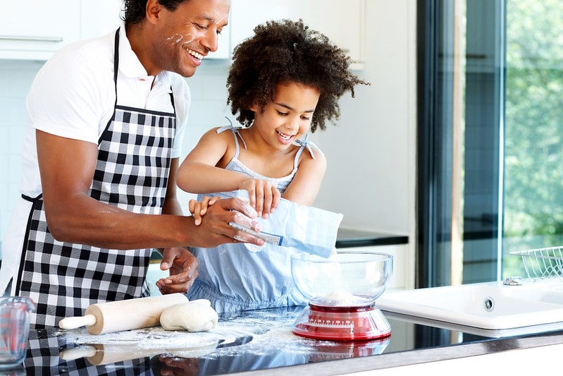 A father and daughter smile as they weigh the amount of flour needed to make a My Little Pony cake.