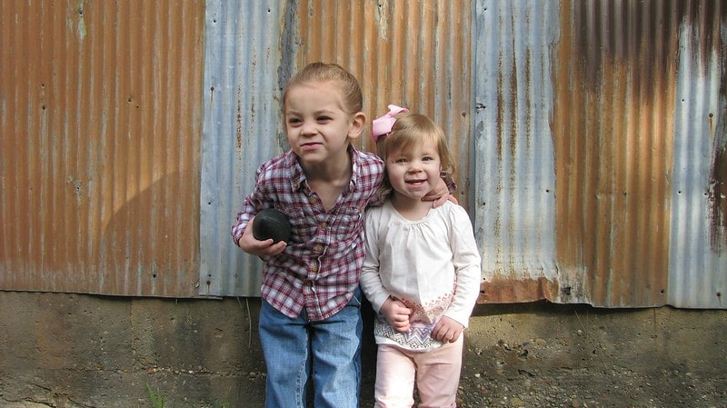 Sisters standing by stables at a farm joking around and pulling faces.