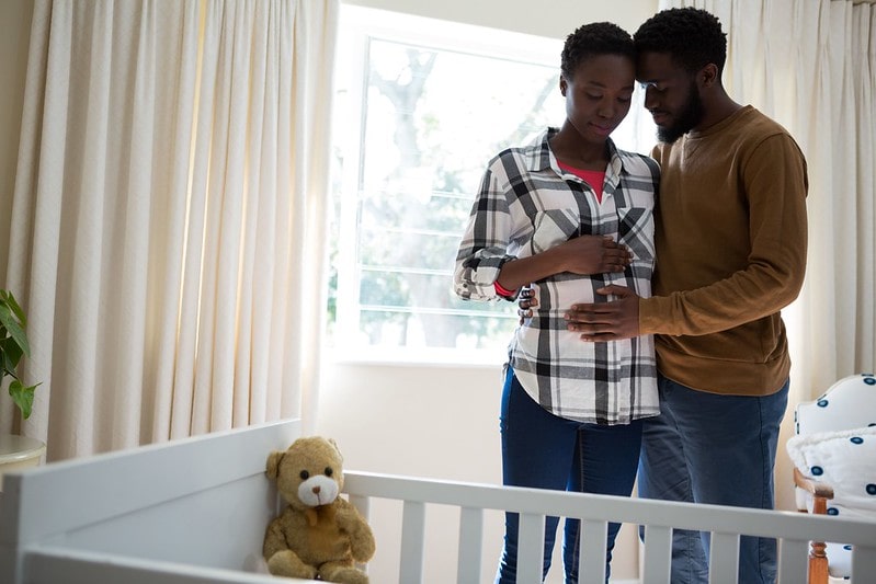 Expecting parents standing next to a crib cradling the baby bump.