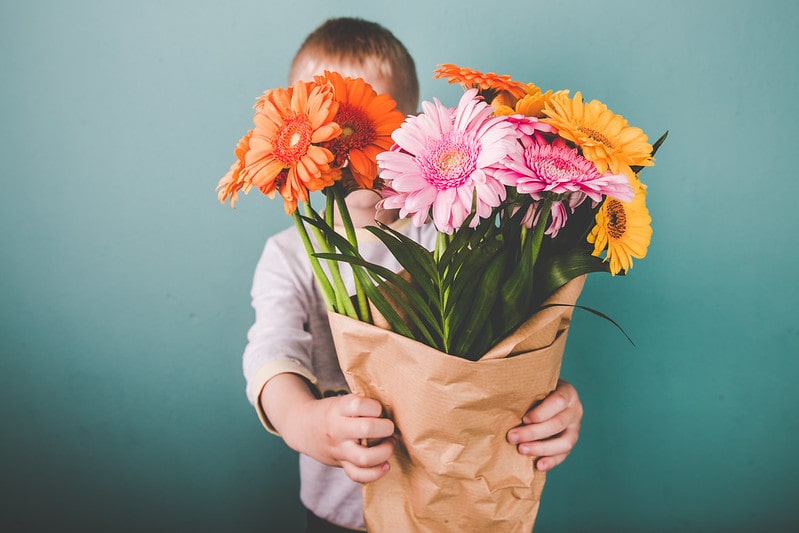 Little boy holding out a bouquet of flowers.
