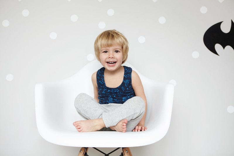 Happy kid sat on a chair in front of wallpaper with the batman logo on it.
