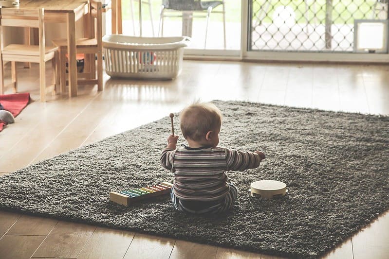 Baby sat on a rug playing with toy musical instruments.