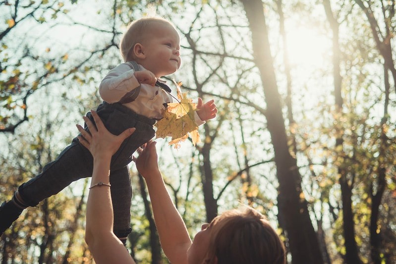 Mum lifting her baby up in the air outside in the park.