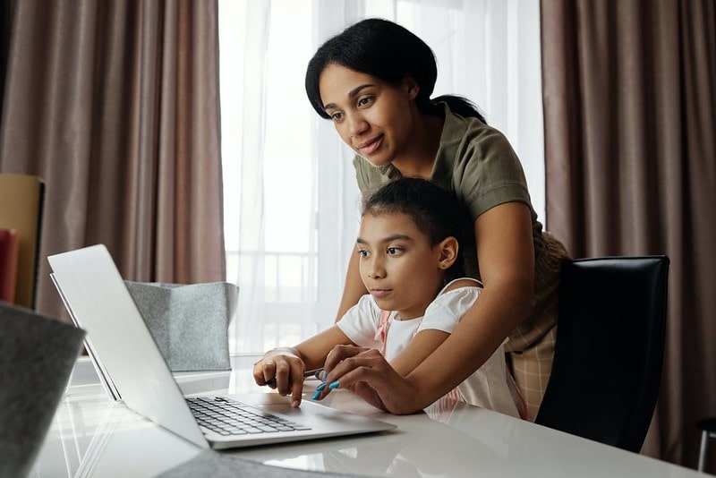 Mum helping her daughter study on her laptop.