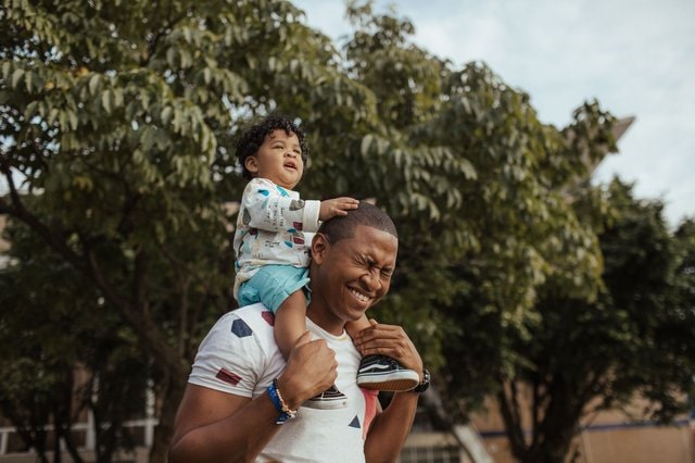 Dad carries baby on on his shoulders smiling.