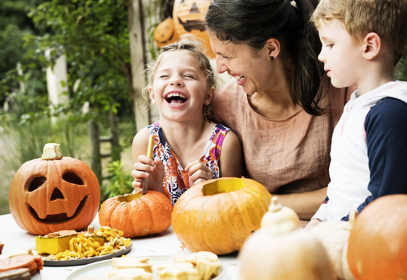 Mum and her kids laughing while carving pumpkins.
