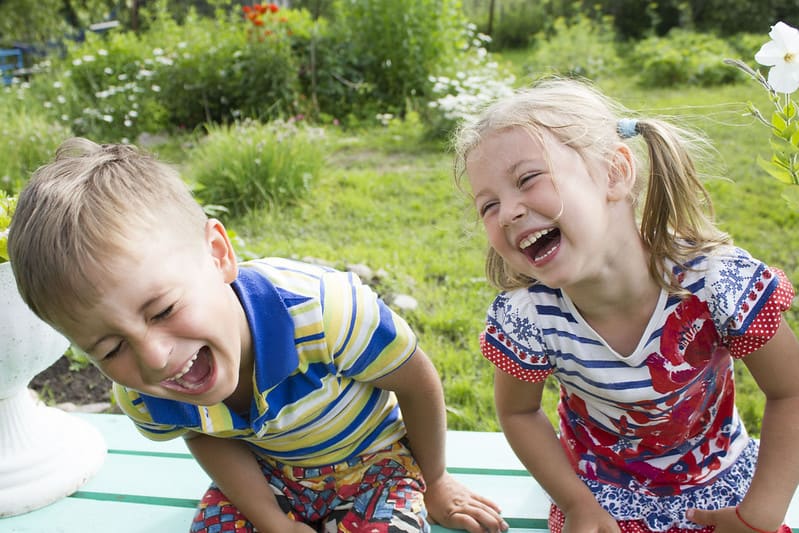Little girl and boy sat on a bench in the garden laughing.