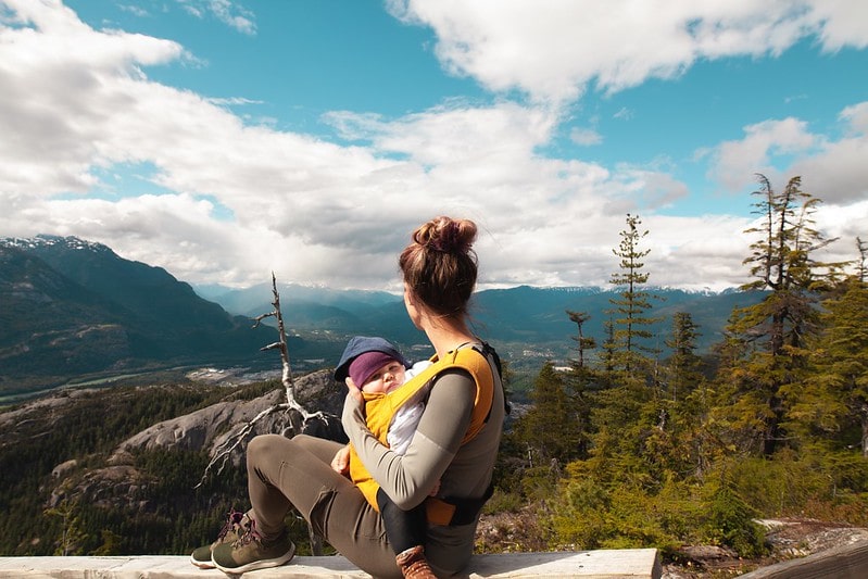 Mum sitting with baby in a baby sling looking out at the view of the mountains.