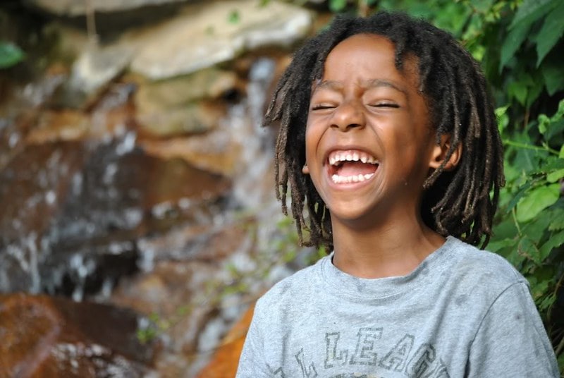 Boy standing outdoors laughing at snail jokes.