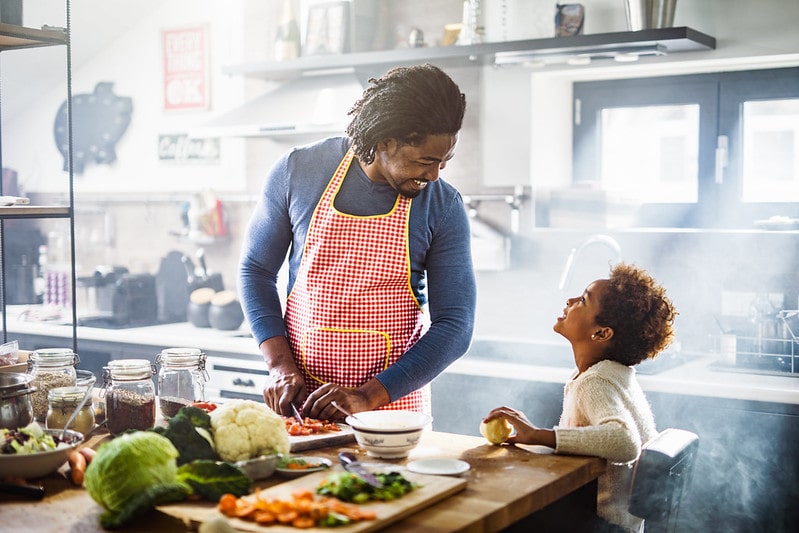 Dad and son in the kitchen laughing as they cook pasta.
