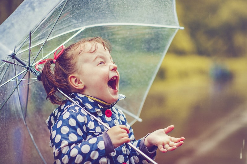 Little girl holding an umbrella laughing as it rains.