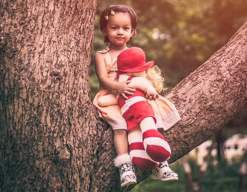 Little girl sat in a tree holding a soft rag doll.