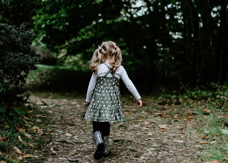 Young girl in a spotty dress walking away through the trees.e