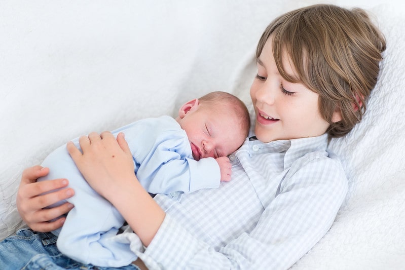 Boy holding sleeping newborn baby brother.
