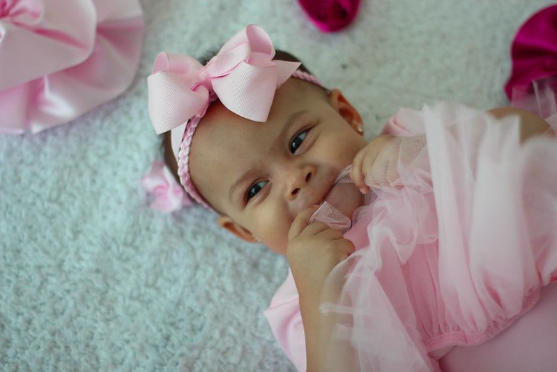 Baby girl wearing a pink bow bow headband, smiling.