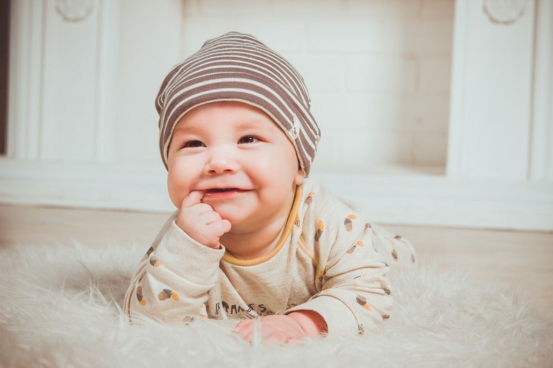 Baby wearing a striped hat lying on a fluffy rug smiling.