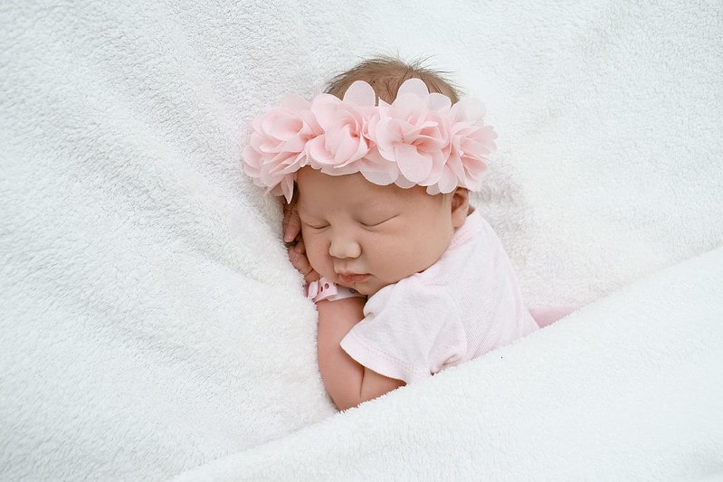 Baby girl wearing a pink flower crown sleeping on the bed.