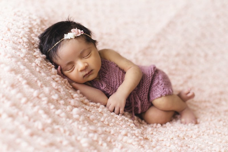 Baby girl wearing a flower headband sleeping on a pink blanket.