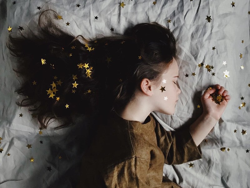 Young girl sleeping on the bed with gold stars on her face, hair and bed.