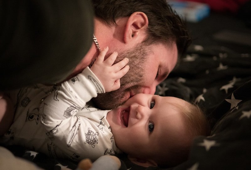 Dad kissing his smiling baby on their cheek, lying on a starry blanket.