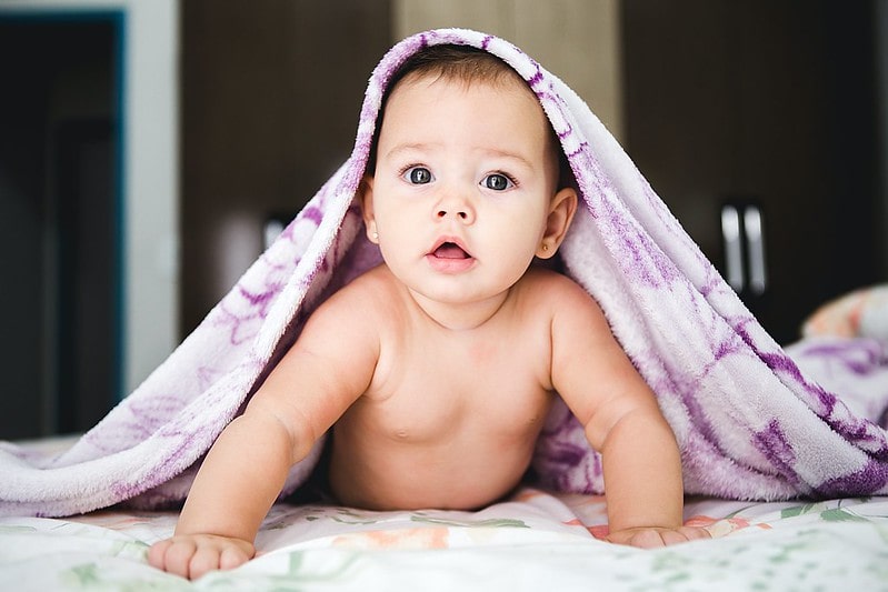 Baby girl peeking out from under a purple blanket.
