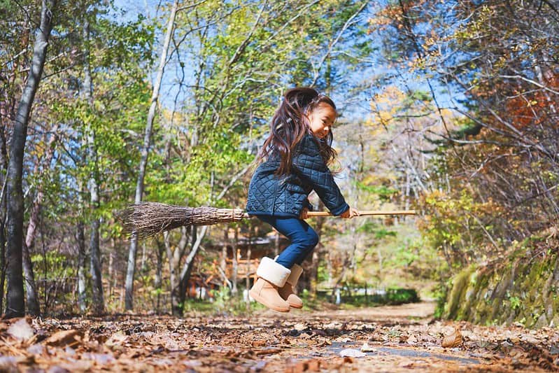 Little girl jumping on a broomstick in the woods.