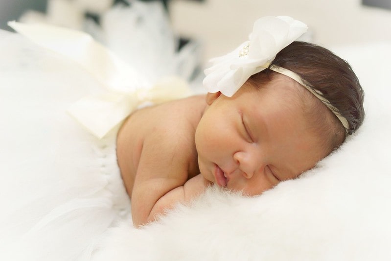 Newborn baby girl wearing a white flower headband sleeping.