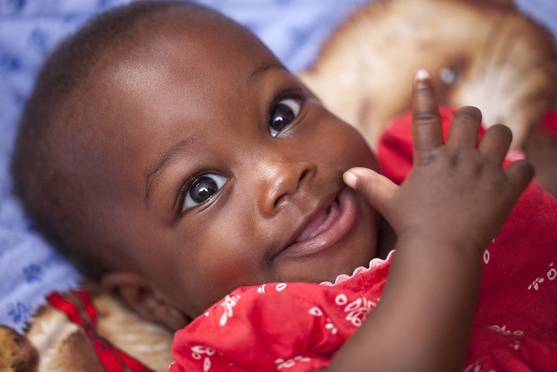 Baby girl wearing a red dress smiling up at her parents.