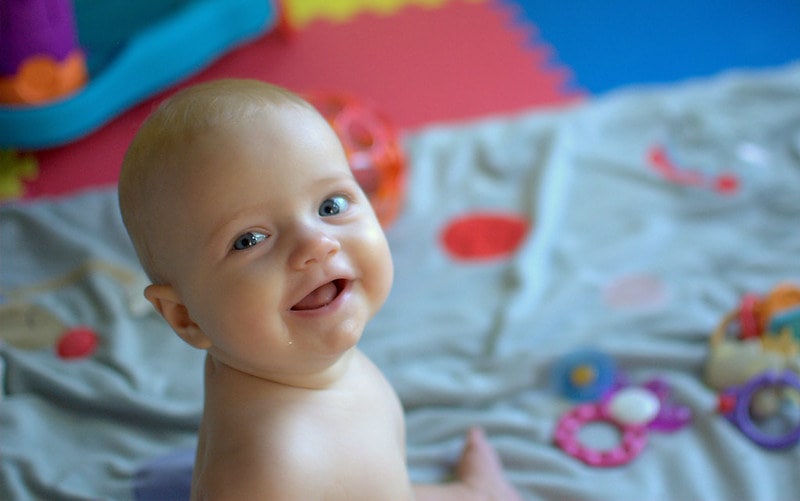 Baby girl smiling sat on a play mat.