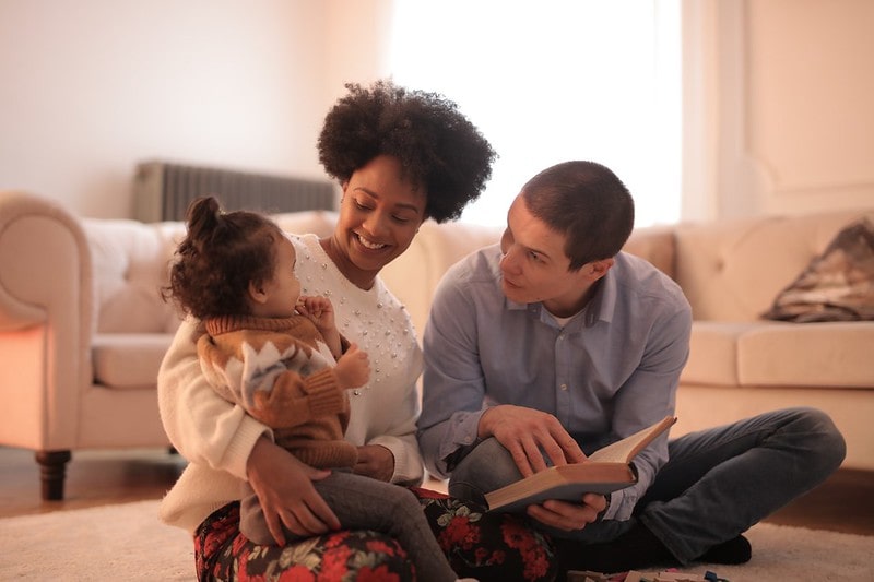Parents reading to their baby girl in the living room.