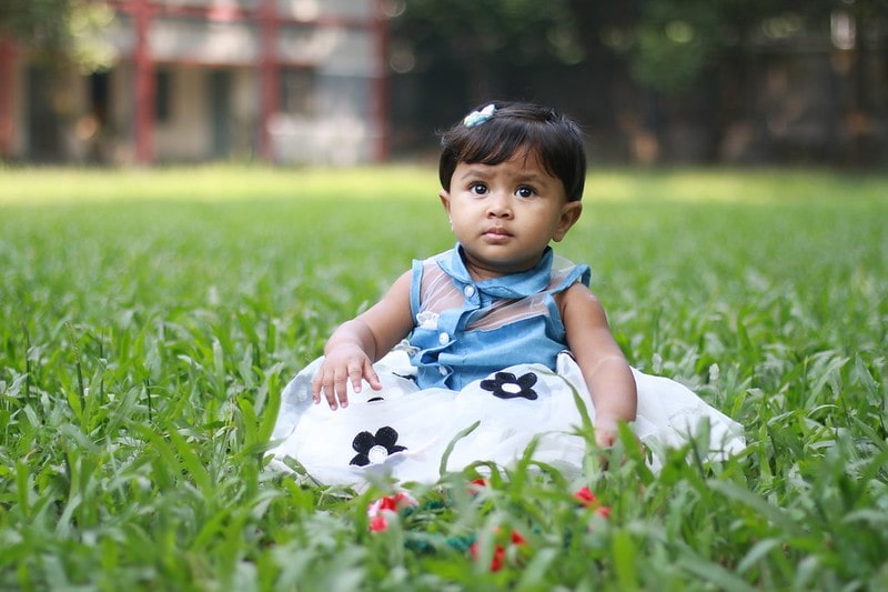 Baby girl in a floral dress sitting in the grass.