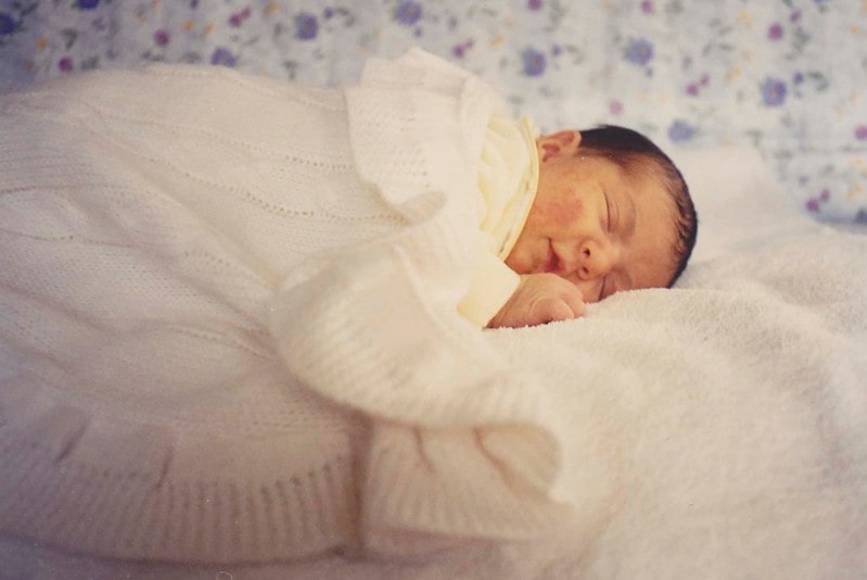Baby fast asleep on the bed covered with a white blanket.