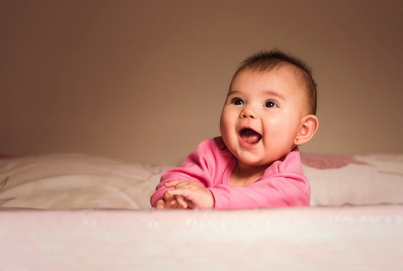 Baby girl wearing pink smiling up at her parents.