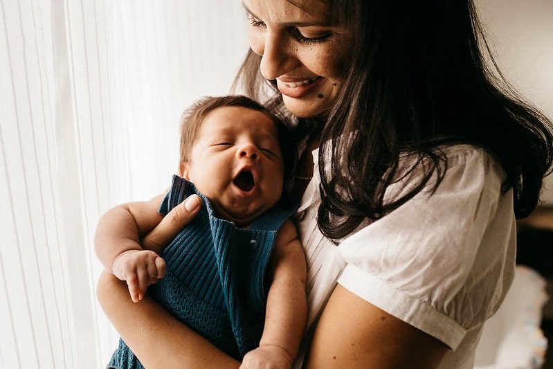 Mother cradling her newborn baby girl who is yawning in her arms.
