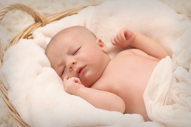 Newborn baby sleeping on a soft white blanket in a moses basket.