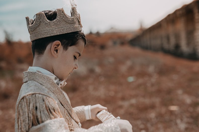Young boy dressed as a prince with a beaded crown and outfit.