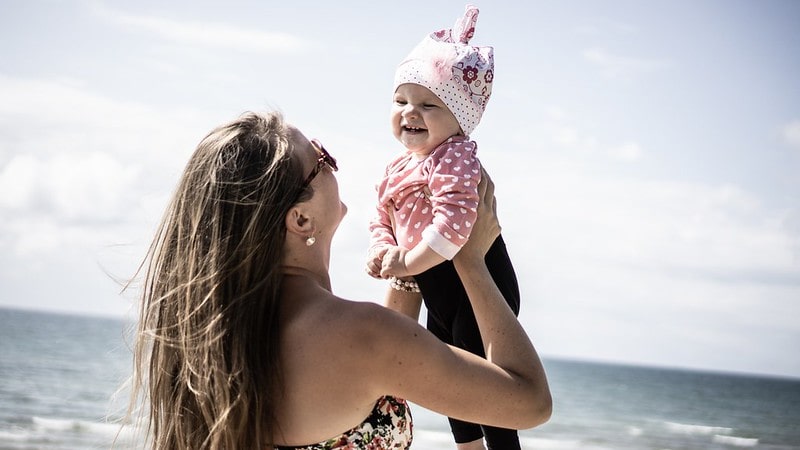 Mum holding baby girl in the air at the beach, both of them happy.