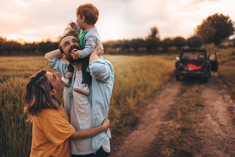 Happy family standing in a field smiling, the baby boy on his dad's shoulders.