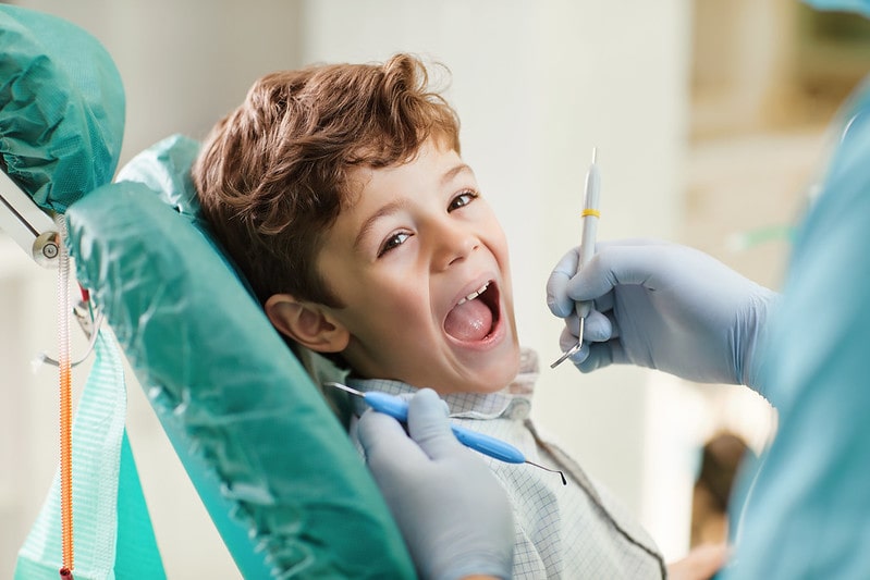 Happy boy at the dentist sitting in the chair with his mouth wide open.