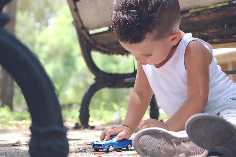 Little boy sat on the floor playing with a blue toy car.