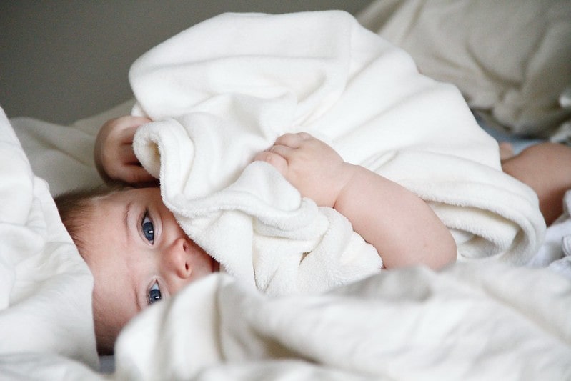 Baby lying on the bed under a white towel.