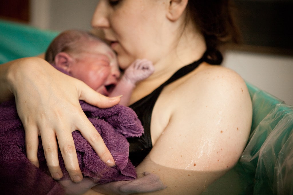 Mum sitting in the birthing pool cradling her newborn baby.