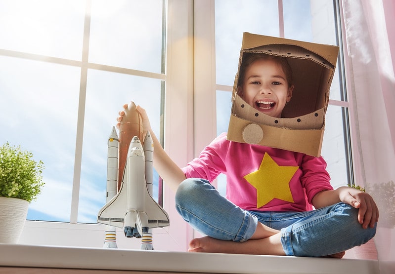 Girl wearing a homemade astronaut costume smiling with a toy rocket in her hand.