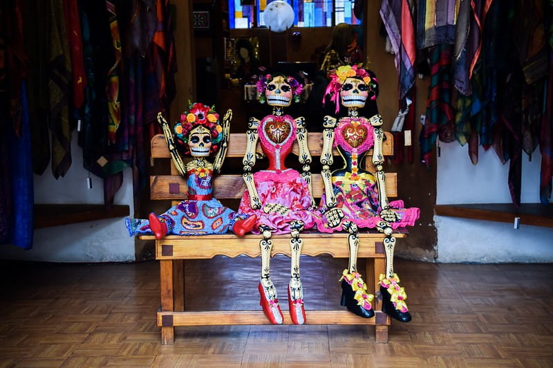 Three skeletons dressed for the Mexican festival 'Día de los Muertos' (Day of the Dead) sitting on a bench.