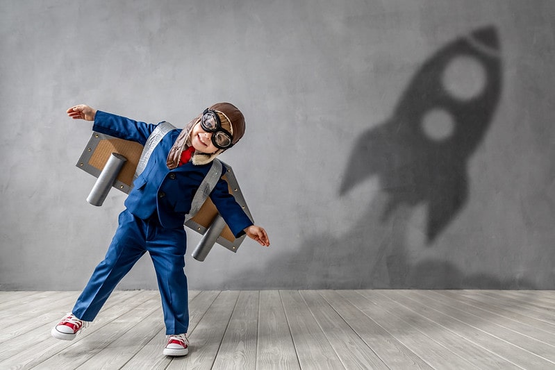Boy smiling in his astronaut costume as a rocket shadow flies on the wall behind him.
