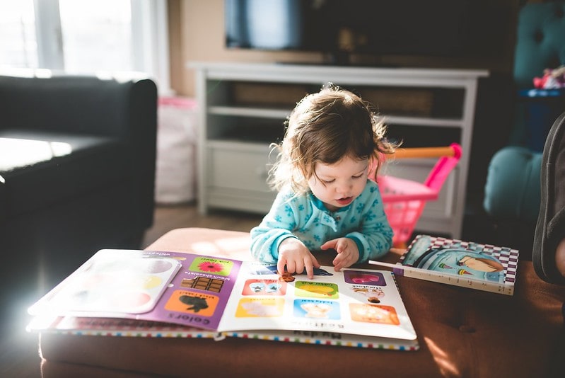 Little girl learning to read, looking at a book on the table.