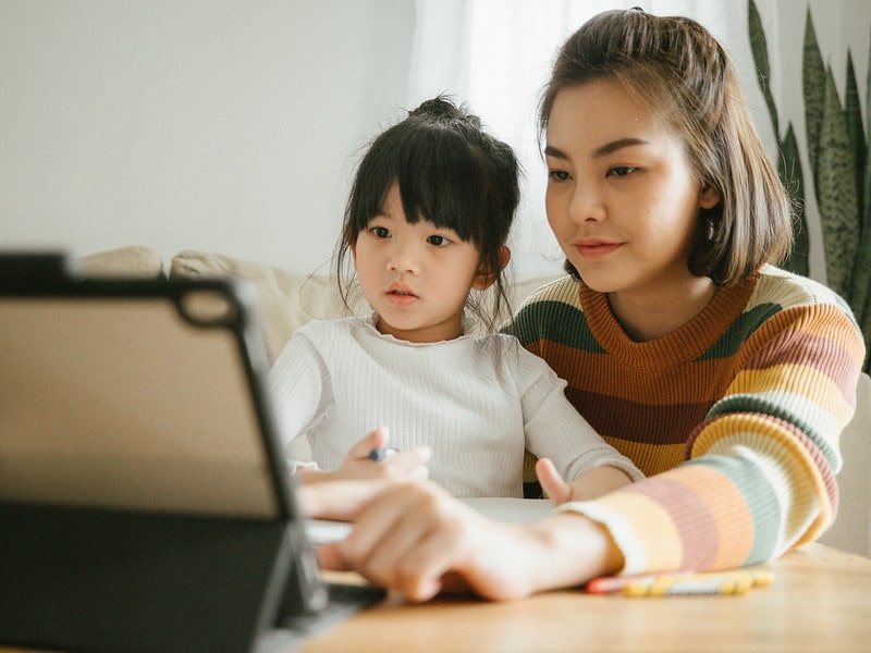 Mum sat with her young daughter showing her how to practise learning words on a tablet.