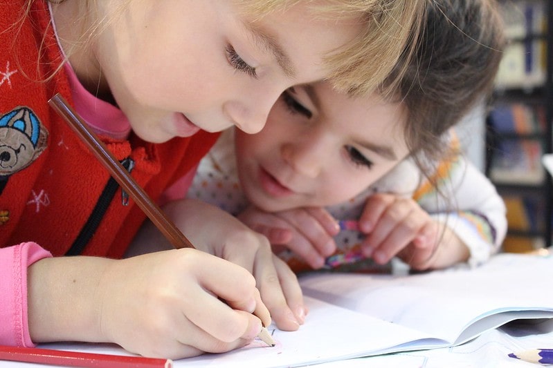 Two girls practising writing words in their workbook at the desk.